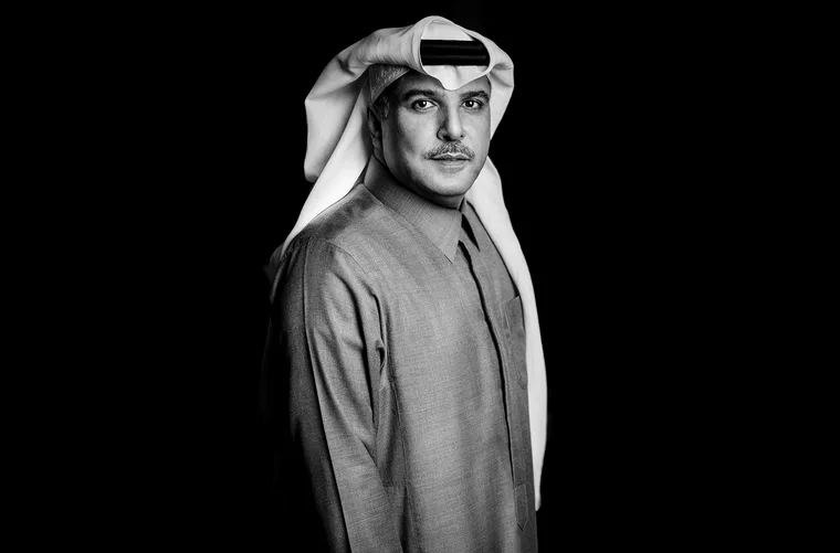 Dramatic black and white portrait of a Saudi man wearing a gray thobe and white ghutra with iqal, standing against a pure black background with striking low-key side lighting highlighting his facial features and composed expression